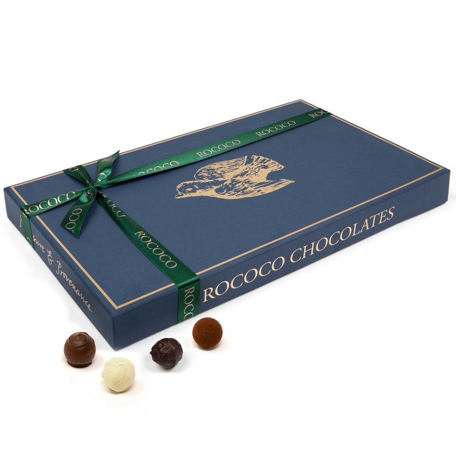 Exquisite collection of 91 Rococo Chocolates truffles, 'A Celebration of Truffles', featuring white, milk, dark, and sea salt caramel flavors, handcrafted in London. Each truffle showcases the art of fine chocolate making, presented in a sophisticated navy box with gold Dove embellishment and tied with a forest green rococo ribbon, ideal for commemorating life's milestones.